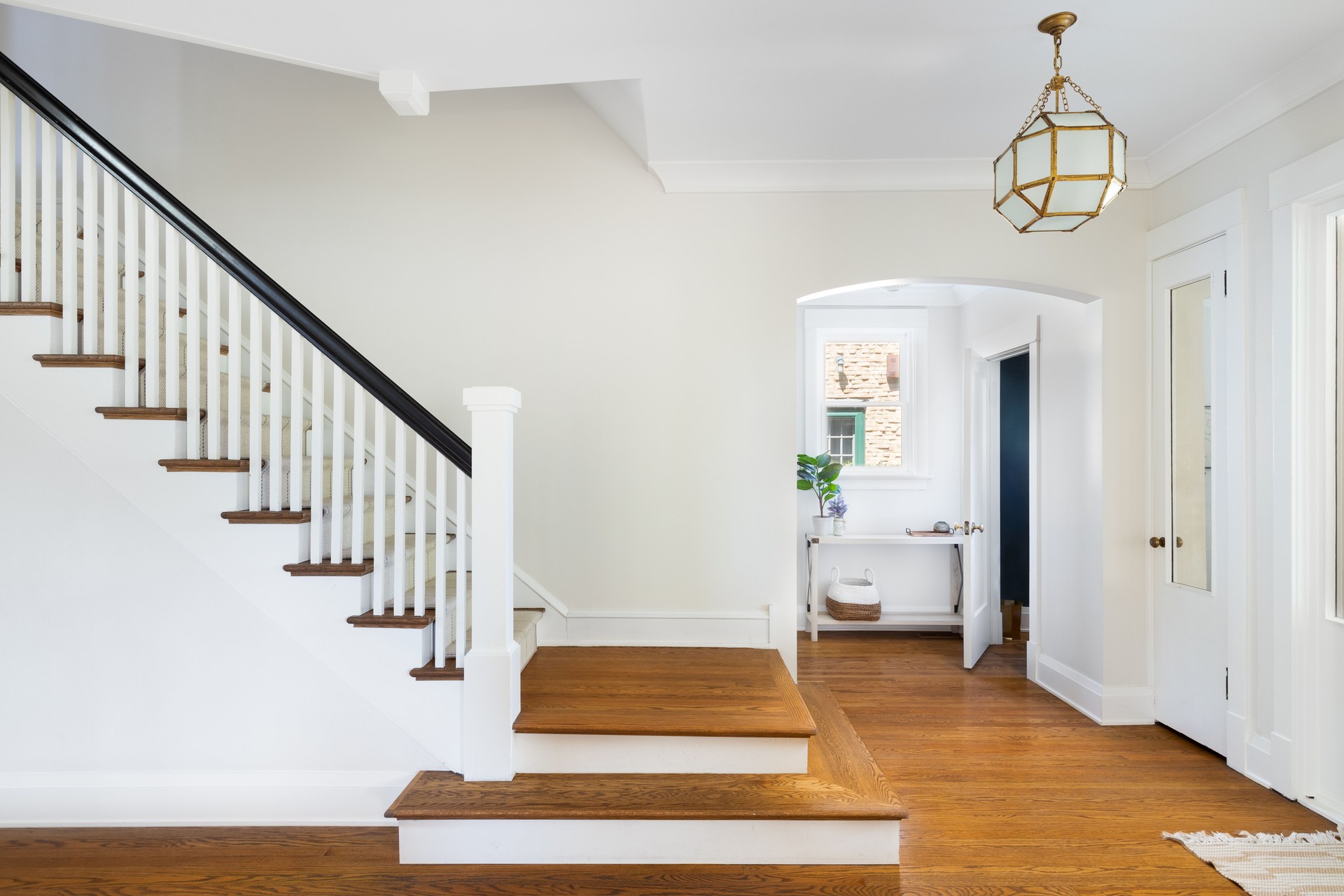 A home's foyer with a renovated staircase and gold light fixture hanging above.